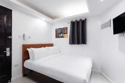 a white bedroom with a bed and a television at Nest Nano Suites Poblacion - Makati in Manila