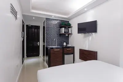 a room with a bed and a kitchen with a tv at Nest Nano Suites Poblacion - Makati in Manila