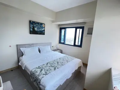 a bedroom with a bed with white sheets and a window at Partial Ocean View Opposite the US Embassy in Manila