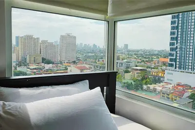 a bedroom with a view of a city from a window at Homes by Gilmore Tower Suites in Manila