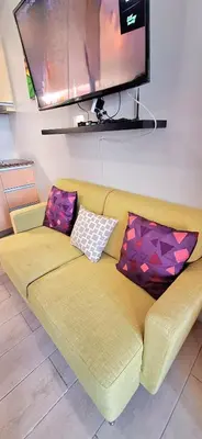 a yellow couch with two pillows and a flat screen tv at Eastwood LeGrand 3 Cozy & Modern Studio Type Condominium in Manila