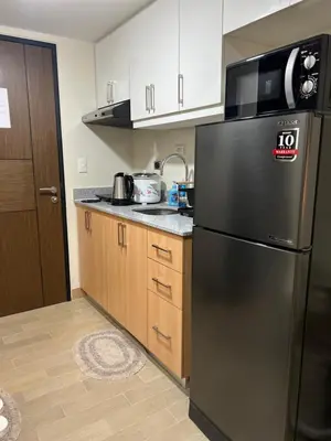 a kitchen with a black refrigerator and wooden cabinets at Brand New Studio w/ Washer in Manhattan Plaza Tower ll in Manila