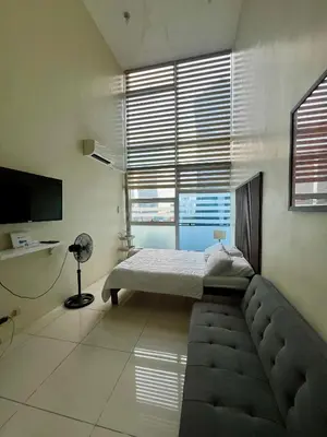 a bedroom with a bed and a couch and a tv at Cozy High Ceiling Studio @ Ortigas near Podium, Megamall in Manila