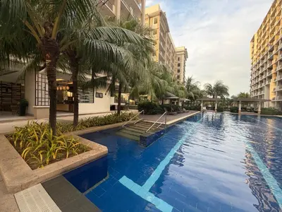 a large swimming pool with palm trees and buildings at Modern style 2BR Condo Good for 6 Packs Near NAIA in Manila