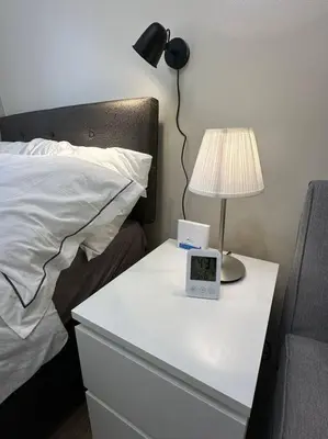 a nightstand with a alarm clock and a lamp on a bed at Affordable Condo Near Nuvali in Silang