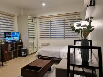 a living room with a bed and a table and a tv at Cute Studio Unit w/ Big Windows - B Morgan T1 in Manila