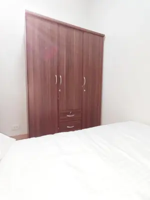 a wooden cabinet in a bedroom with a white bed at Condo near Mall of Asia in Manila