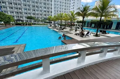 a large swimming pool with palm trees and a large building at Meowcation Condo in Makati in Manila