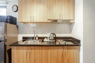 a kitchen with wooden cabinets and a sink at ClaySky Staycation S2T1-Cozy & Homey 1BR Apartment near MOA facing Pool with Own Parking with Netflix, HBO Max YouTube Premium & up to 200mbps Wifi in Manila