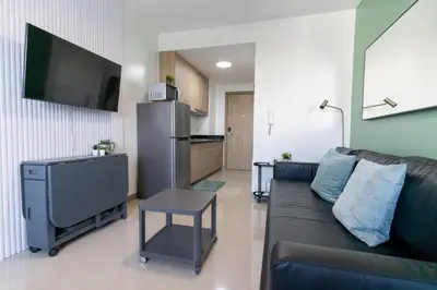 a living room with a couch and a tv and a kitchen at Concrete Palms near MOA w/ awesome view of Manila in Manila