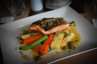 a white plate with a piece of fish and vegetables at Amelie Hotel Manila in Manila