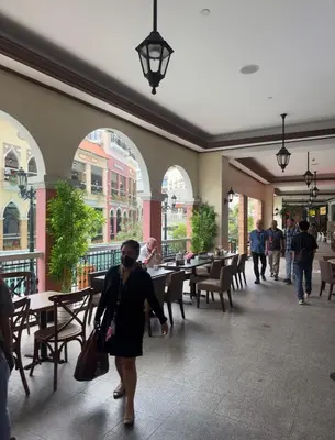 a woman walking through a restaurant with tables and chairs at Amazing Sunrise Venice Grand Canal Balcony, Xbox Series X console with Game Pass Ultimate, FREE coffee, Pool, Gym & Sauna, 5 mins to BGC in Manila