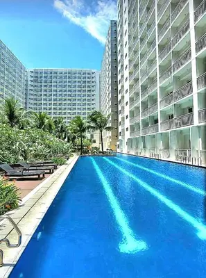 a large swimming pool in front of a large building at California Suite - by GUEST RESERVATION'S MANILA in Manila