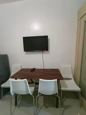 a dining room table with white chairs and a television on a wall at 1BR SEA RESIDENCE by ABBY in Manila