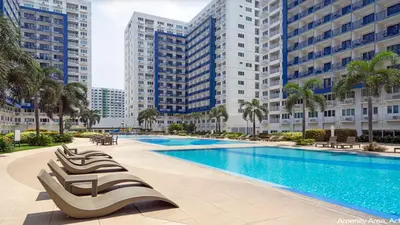 a swimming pool with chaise lounge chairs in front of tall buildings at SEA 2-BR Unit with Free Parking near Mall of Asia in Manila