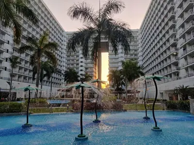 a swimming pool with umbrellas in front of tall buildings at Shell Residences Condo Suite Staycation near MOA and Airport in Manila