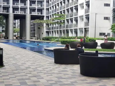 a building with a swimming pool and people sitting on benches at JoVis Place Staycation near MOA(Wifi & Netflix) in Manila
