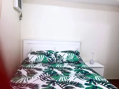 a bed with a green and white comforter and pillows at Lovely two bedroom apartment with balconies in Manila