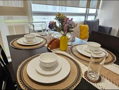 a table with plates and bowls and a vase with flowers at Sunshine 100 Plaza - Bright and cozy 1 bedroom with washer in Manila