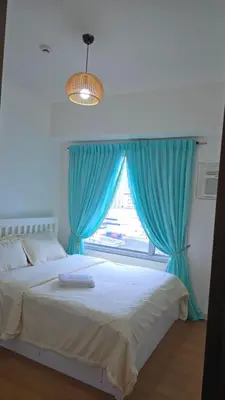 a bedroom with a bed with blue curtains and a window at 8 Adriatico Condotel Unit Facing Manila Bay in Manila