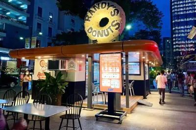 a restaurant with a donut sign on a city street at BGC Staycation: 1BR Condo Uptown Area #ournw12d in Manila