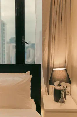 a bed with a lamp on a night stand next to a window at The Skyline Oasis Makati in Manila