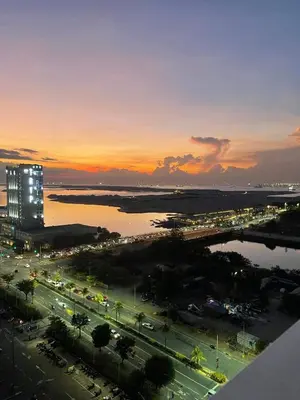 a sunset over a city with a building and the water at Shore Residence Manila Bay City Lights View MOA Complex in Manila