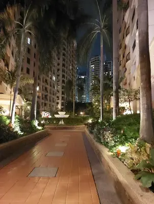 a walkway in a city at night with palm trees at 1BR Condotel - Forbes Town Road near St Lukes BGC Taguig in Manila