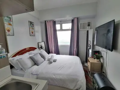 a bedroom with a white bed and a television at Dens condotel Metro Manila in Manila