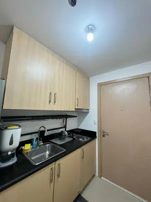 a kitchen with wooden cabinets and a sink and a door at Cozy condo by the MRT & Light Mall experience comfort and convenience in Manila
