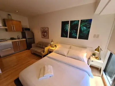 a bedroom with a large white bed and a kitchen at Scandi Inspired Studio in Knightsbridge, Makati in Manila
