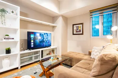 a living room with a couch and a tv at Avant at the Fort BGC 1BR Flr to Ceiling Cor Unit with Great View in Manila