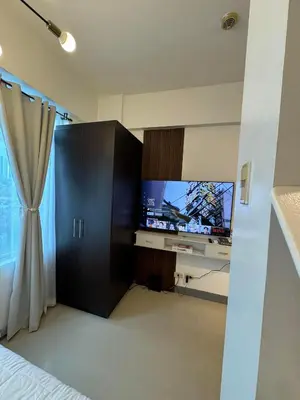 a living room with a tv and a curtain at Your perfect retreat in Stamford! Enjoy our stylish, fully furnished studio just steps away from the vibrant Venice Mall in Manila