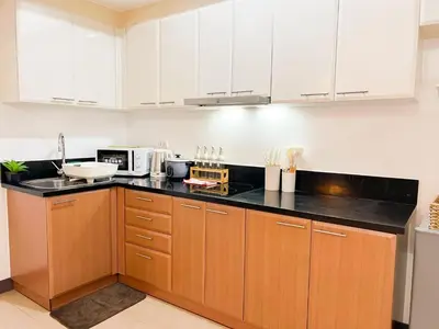 a kitchen with white cabinets and a black counter top at Modern BGC Stay at Venice Residences #vlrtc29h in Manila