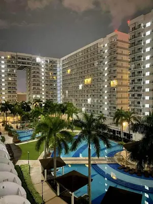 a large building with a swimming pool and palm trees at Condotel By RhoiVC in Shell Residences Moa Near Naia Airport in Manila