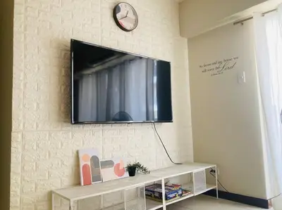 a flat screen tv on a wall with a shelf at Cozy 3 Bedroom Staycation near BGC Makati Airport in Manila