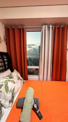 a bedroom with a bed with an orange comforter and a window at Sophia's Place Beacon Amorsolo in Manila