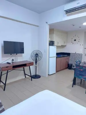 a living room with a table and a television and a kitchen at Jennie's 5m Suite in Manila