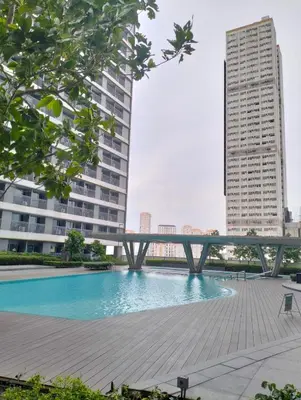 a bridge over a swimming pool with two tall buildings at Ortigas Greenfield Cozy Lodge in Manila