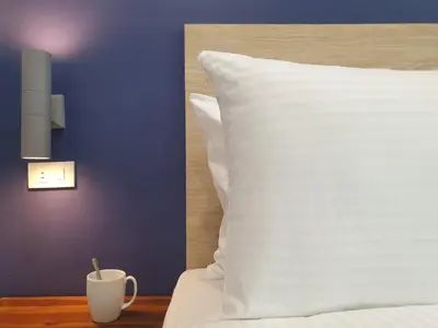 a bed with a white pillow and a cup on a table at Leez Inn Makati in Manila