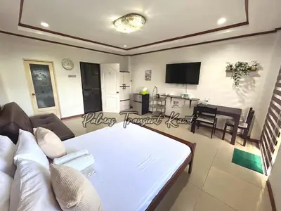 a living room with a white bed and a kitchen at Palmas Transient Kawit in Kawit