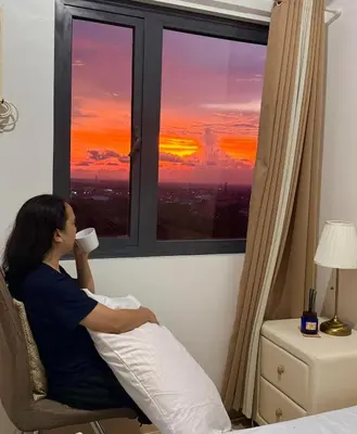 a woman sitting in a chair drinking a cup of coffee looking out a window at Green 2 - Gems Suite in Dasmariñas