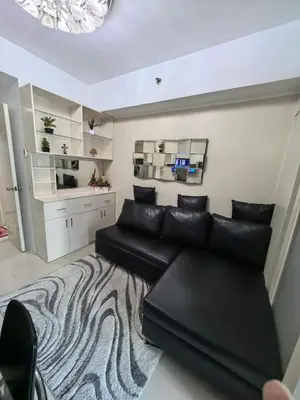 a living room with a black leather couch and a rug at Athalia's Pad at Sea Residences in Manila