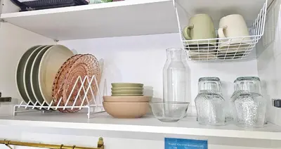 a shelf with plates and glass bottles on it at The Cozy Hub Studio with Wifi Near Eastwood City in Manila