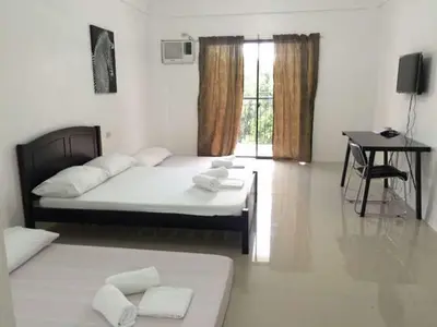 a bedroom with two beds and a desk and a table at The Palines Apartment Hotel near Brittany Palazzo Villar City in Manila