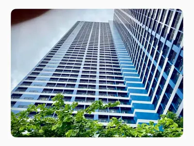 a tall building with blue windows and trees in the foreground at Chic Luxury Air condo 2 Bedroom Finest City Living Air Makati Gym Swim Park 300 in Manila