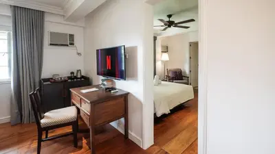 a hotel room with a bed and a desk with a television at MiraNamin Nest LIRYO and LANTANA - Luxury Residence in Unique Historic Home - Indoor Plunge Pool, Self-Service Breakfast, Garden View, Rooftop, Private Kitchen in Manila