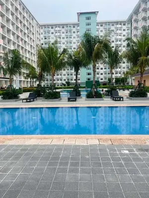 a swimming pool with palm trees in front of a building at Field Residences Condo Hotel Near Manila Airport in Manila