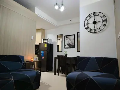 a living room with a clock and a table and chairs at Shore Residences - 2 Bedroom Pool View Near Moa in Manila