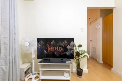 a living room with a tv on a stand with a desk at Forbeswood Heights 1Br with Garden view in Manila